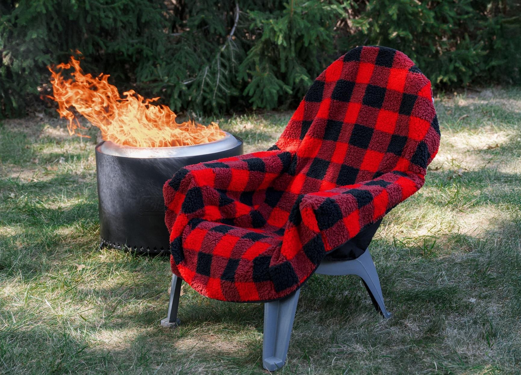 A single outdoor chair covered with a red and black blanket next to a fire pit